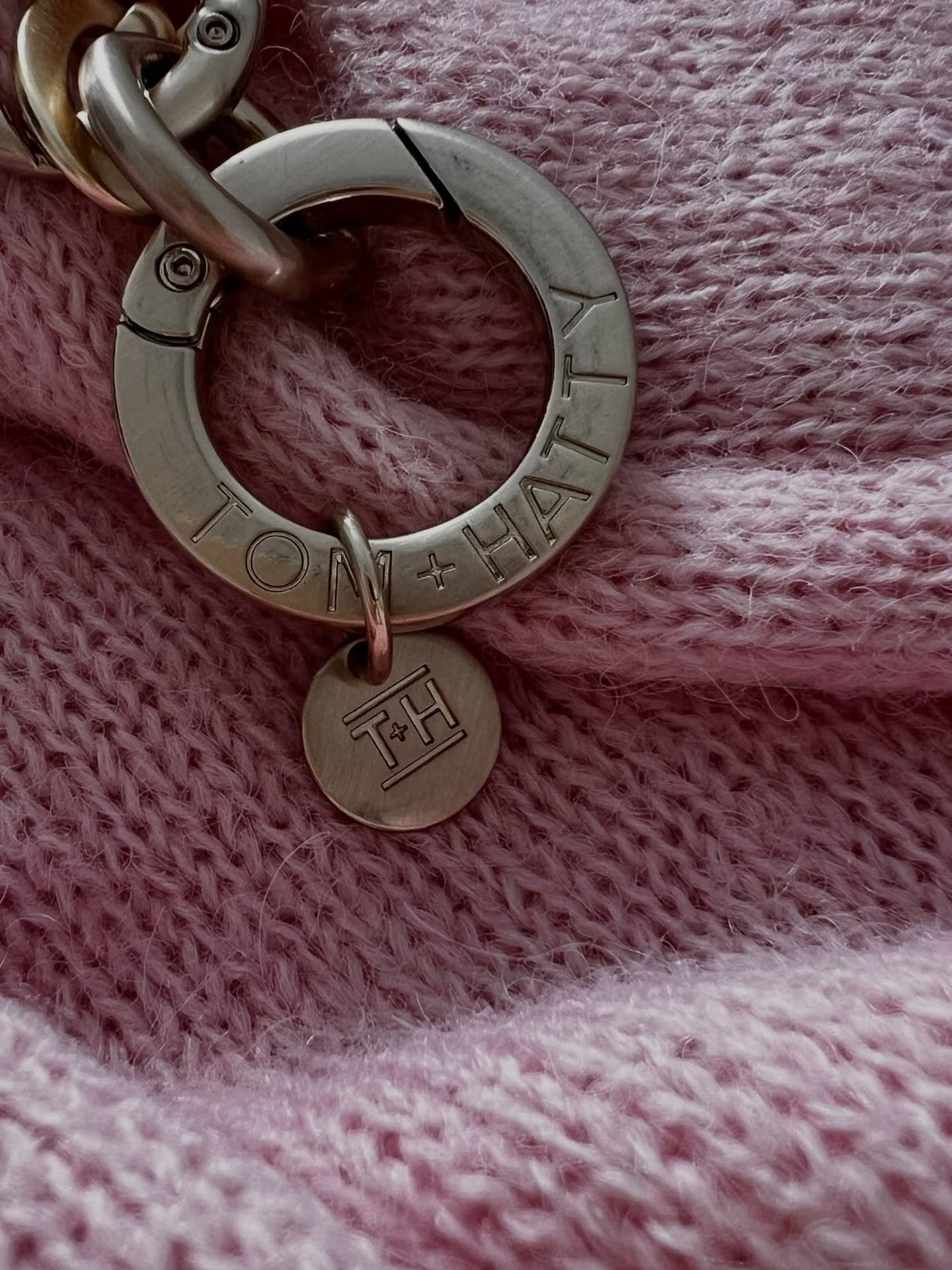 Nahaufnahme eines silbernen Anhängers mit Gravur auf rosa Strick